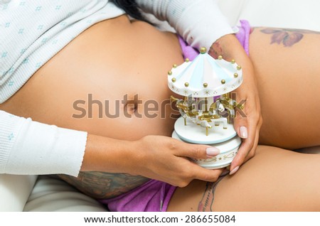 caption of pregnant belly sitting down and hands holding a small carousel