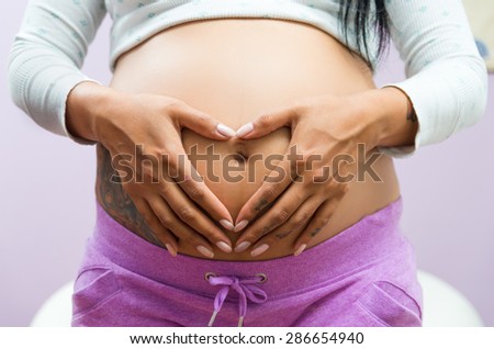 caption of pregnant belly with tattoos and hands resting on stomach