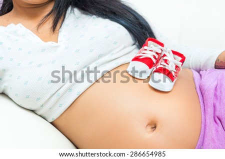 caption of pregnant belly of woman lying sideways with converse baby shoes sitting on stomach