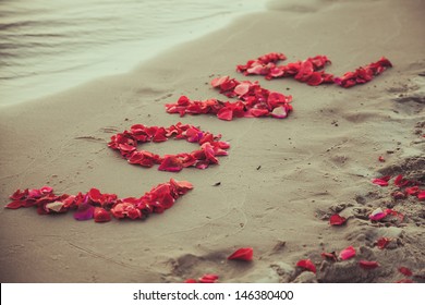 Caption word love in the sand of the sea. Love inscription from the petals of roses.