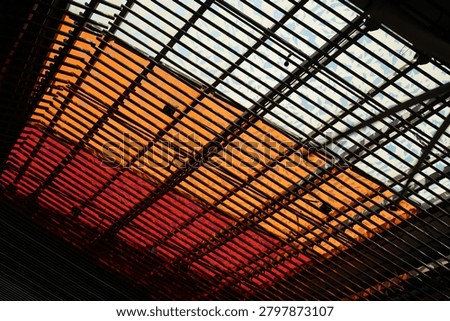 A captivating abstract view of an architectural ceiling design. The structure features a mix of orange, red and white hues, creating a warm and dynamic visual experience.