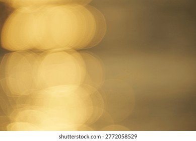 A captivating array of golden bokeh lights creates a soft, abstract reflection on a surface. This warm and blurry image offers a tranquil background for various artistic and design projects.