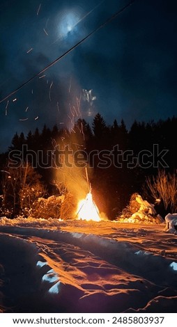 A captivating bonfire blazing under a dark night sky in a snowy landscape, creating a mesmerizing and warm scene ideal for winter themes or adventure content.