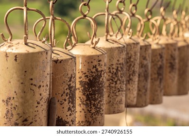 A captivating close-up of a weathered row of rustic metallic bells, displaying aged golden-brown tones and intricate speckled textures. These traditional chimes evoke a sense of ancient craft and
