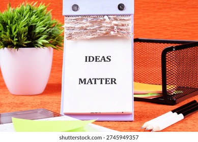 A captivating desk setup featuring a white flip calendar with the inspiring words Ideas Matter amid a lush green plant and organized stationery.