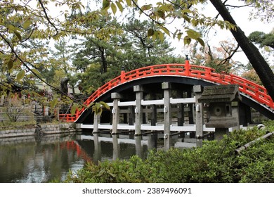 Captivating images of popular locations in Osaka, Japan, showcasing Sumiyoshi Taisha, an ancient shrine, with a striking red arch bridge elegantly mirrored on the tranquil water surface. - Powered by Shutterstock