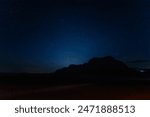Captivating night sky, sprinkled with stars sets over the silhouette of Jabal al Qattar rock formation in the tranquil Wadi Rum desert in Jordan in April