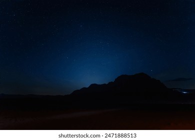 Captivating night sky, sprinkled with stars sets over the silhouette of Jabal al Qattar rock formation in the tranquil Wadi Rum desert in Jordan in April - Powered by Shutterstock