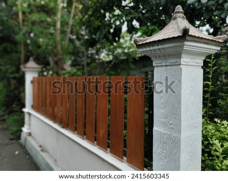 A captivating photo showcases a house fence featuring white concrete pillars adorned with a touch of natural elegance. The center of attention is the brown wooden plank that runs through the middle