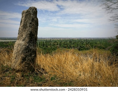 A captivating photograph capturing the essence of an ancient stone pillar standing against the clear day sky, with a distant horizon seamlessly blending a lush forest and a clear sky.