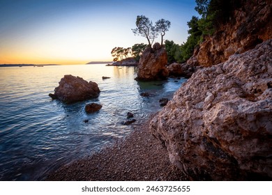 A captivating photograph of a tranquil coastal sunset over a rocky shoreline. The image captures the serene beauty of the calm ocean waters reflecting the warm hues of the setting sun. - Powered by Shutterstock
