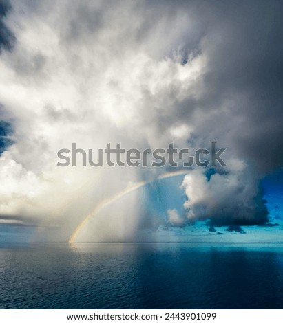 A captivating seascape featuring a vivid rainbow arching gracefully against dramatic clouds, illuminating the serene ocean below. This awe-inspiring image is perfect for travel, environment, and inspi