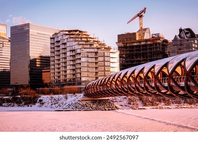 Captivating sunset cityscape featuring a distinctive red pedestrian bridge over a frozen river in Calgary, Alberta. The scene includes contemporary buildings and construction cranes. - Powered by Shutterstock
