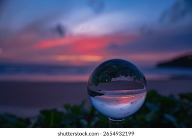 A captivating sunset reflected through a crystal ball, creating an inverted and artistic perspective of a serene beach scene at dusk. sweet sky in sunset over the sea background.