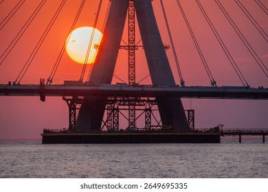Captivating sunset view of the under-construction Danshui cable bridge in New Taipei Taiwan, with the sun setting behind the structure, casting a warm glow over the water.