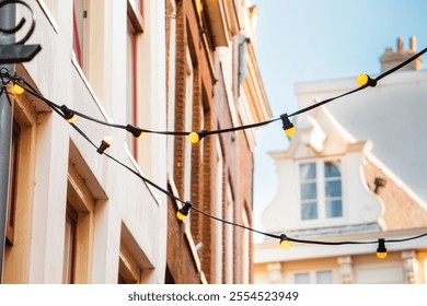 Captivating urban landscape showcasing string lights hanging between historical buildings. The warm glow creates a welcoming and festive atmosphere against the blue sky. - Powered by Shutterstock