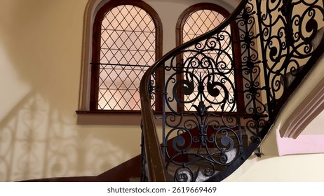 The captivating view of an elegant staircase features intricate ironwork and beautifully designed windows