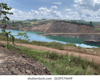 A captivating view of a former mining pit transformed into a tranquil turquoise lake surrounded by green hills and dramatic rock formations.