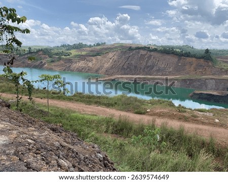 A captivating view of a former mining pit transformed into a tranquil turquoise lake surrounded by green hills and dramatic rock formations.