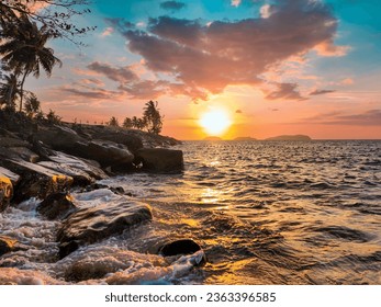 Capture Beautiful Sea Scape and half Landscape in Beautiful Sunset. The photo with thousands stories. Sunset photo. sea water and reflection. Rocks, Grass, and coconut trees beside the beach.