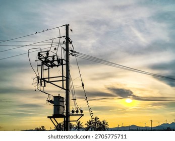 Capture the dramatic visual contrast of electrical transformers against a stunning sunset sky, exploring their critical role in power distribution and electrical engineering.
