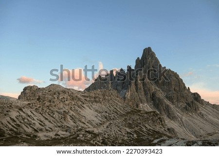 A capture of high and sharp peaks of Dolomites in Italy during the golden hour. The sky is full of soft clouds. Lots of lose stones and pebbles. Raw and desolated landscape. Serenity and calmness