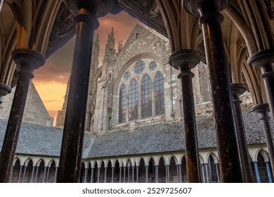 Capture the serene beauty of Mont Saint-Michel Abbey at sunset, showcasing Gothic architecture, medieval stonework, and a peaceful cloister view framed by arches. Ideal for travel and heritage lovers. - Powered by Shutterstock