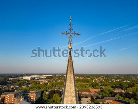 Captured from an aerial perspective, this image features the spire of a church with an ornate cross perched atop, reaching towards the vast blue sky. The spire stands as a poignant symbol of faith and