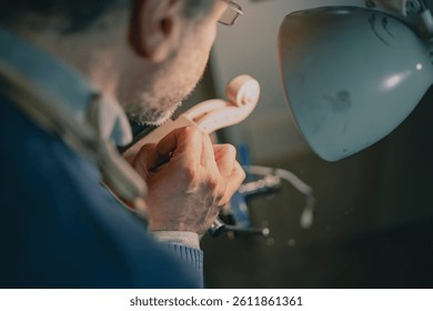 Captured in a Cremonese workshop, this luthier uses a chisel to shape a violin scroll. Wearing glasses and a leather apron, his steady hands reflect years of artisan violin-making experience. - Powered by Shutterstock - Get 15% off with code: PIKWIZARD15