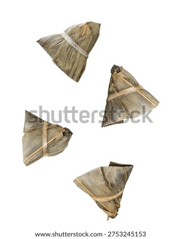 Captured in a dynamic, eye-catching composition, four individual Zongzi parcels are artfully suspended mid-air against a stark white background. Each Zongzi, a traditional Chinese delicacy of glutinous rice wrapped in bamboo leaves, is tied with string, showcasing its characteristic triangular shape and textured wrapping. This unique presentation makes the image ideal for food-related websites, culinary blogs, advertising campaigns for Asian restaurants, or articles discussing food culture and traditions.