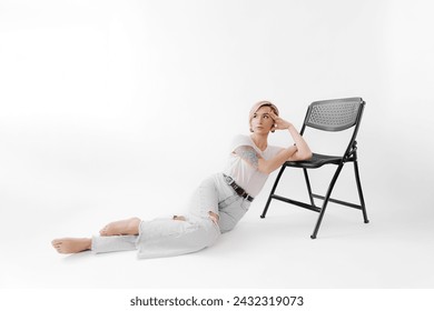 Captured in thought, a young woman rests against a chair in light denim, contemplating in a serene studio space - Powered by Shutterstock