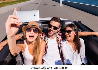 Capturing bright moments. Top view of three young happy people enjoying road trip in convertible and making selfie