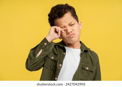 Capturing children's feelings. A small sleepy African American child in stylish wear, squints and wipes an eye, isolated on a cheerful yellow background - Powered by Shutterstock