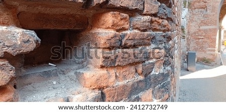 Capturing the clash of history and dirt, an ancient brick wall, marred with graffiti and cigarette butts. A modern trash bin and arch in the background