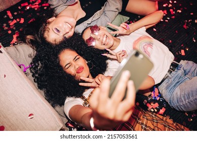 Capturing Crazy Party Moments. Top View Of Three Happy Friends Taking A Selfie While Lying On The Floor At A House Party. Group Of Cheerful Female Friends Having Fun Together On The Weekend.