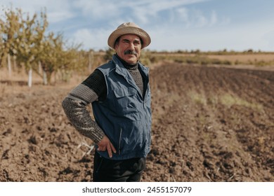 Capturing the Essence A compelling portrait of a seasoned senior farmer, embodying wisdom and experience, set against the picturesque backdrop of an expansive agricultural field. - Powered by Shutterstock