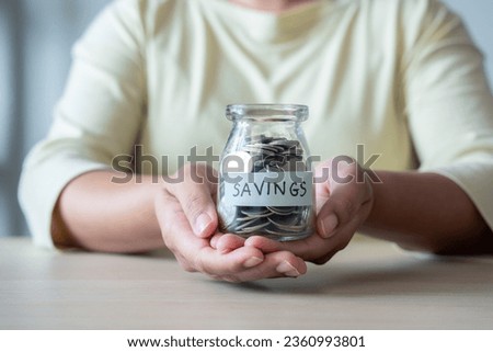 Capturing the essence of financial prudence, a woman placing a coin into a jar, the journey of saving money. Commitment to achieving financial goals through patience and consistent effort.
