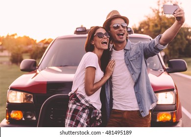 Capturing fun. Beautiful young couple bonding to each other and leaning at their pick-up truck while making selfie