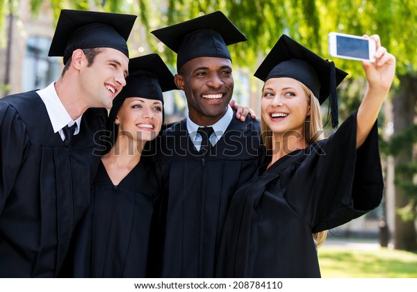 Capturing a happy
moment. Four college graduates in graduation gowns standing close
to each other and making
selfie