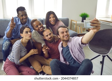 Capturing Life Moments With Modern Technology: Diverse Group Of Six Happy Young Friends Taking Selfie Looking At Phone Screen With Funny Grimace Face Expressions During Small Gathering In Living Room