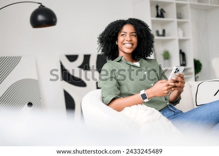 Capturing a moment of genuine happiness, an African-American woman interacts with her smartphone, possibly sharing good news or enjoying a humorous conversation in a tasteful and contemporary living
