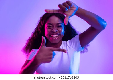 Capturing moments. Happy black woman making picture frame with fingers, looking at camera and smiling for photo in neon light. African American lady showing photograph gesture - Powered by Shutterstock