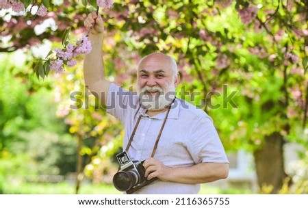 Capturing moments that captivate your heart. Photographer filming. Perfect frame. Pension hobby. Senior man photographer blooming trees background. Cameraman retirement. Professional photographer