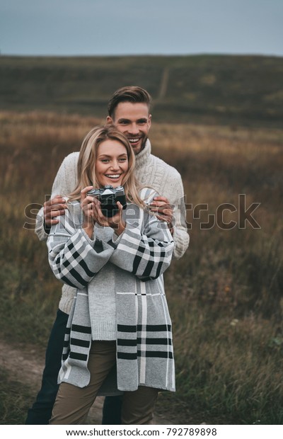 Capturing nice view.\
Beautiful young woman looking away and smiling while standing with\
her boyfriend\
outdoors