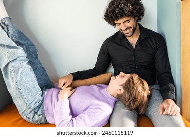 Capturing a serene moment, this image features two friends in a comforting and casual environment. An androgynous person wearing a lavender sweater lies down with legs up against the wall, while a - Powered by Shutterstock