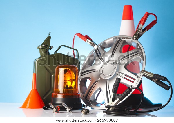 Car accessories - an alloy wheel with
traffic cone and jump start cables with canister of fuel, orange
funnel and amber beacon light on blue
background