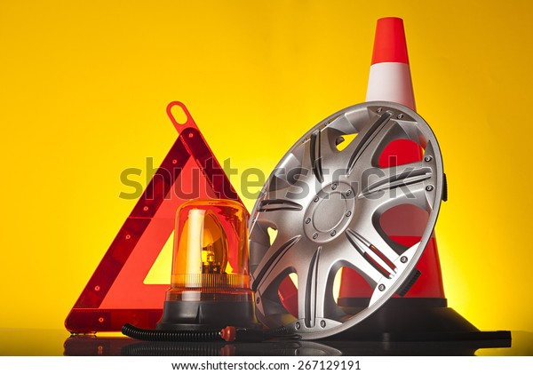 Car accessories - emergency vehicle amber\
beacon flashing light with road triangle and traffic cone with car\
hubcap on yellow background