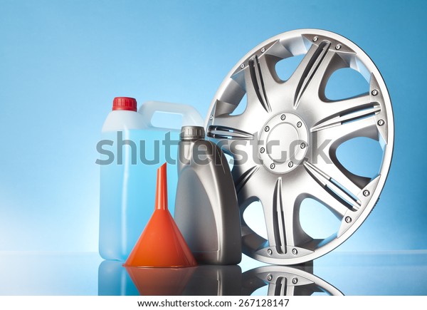 Car accessories - orange funnel with car\
liquids and car hubcap on blue\
background