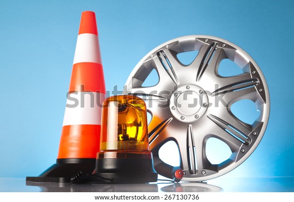 Car accessories -\
traffic cone with emergency vehicle amber beacon light and car\
hubcap on blue background