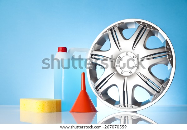 Car\
accessories - yellow car-wash sponge with washer fluid and orange\
funnel next to car hubcap on blue\
background